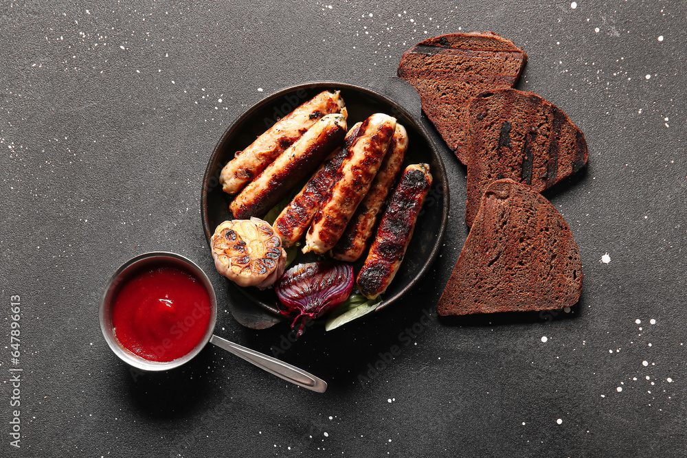 Frying pan of tasty grilled sausages, sauce and bread on black background