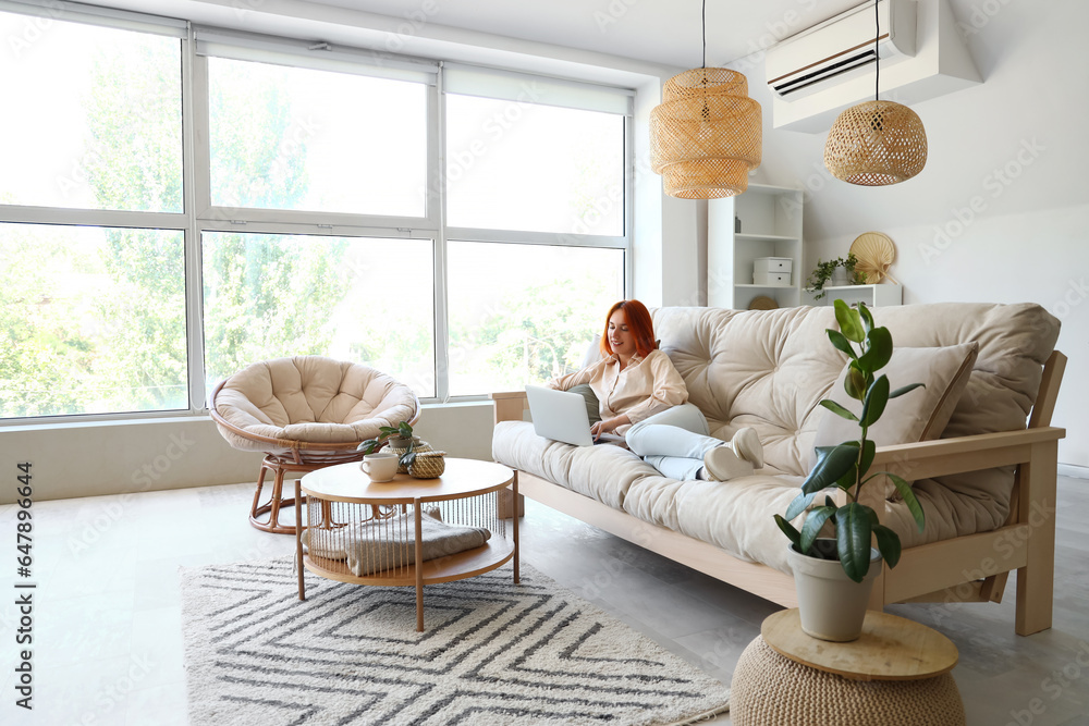 Young woman using laptop on couch in living room