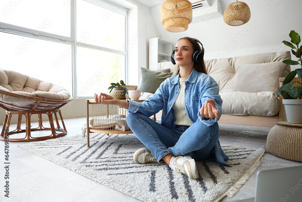 Young woman with headphones meditating on carpet in living room