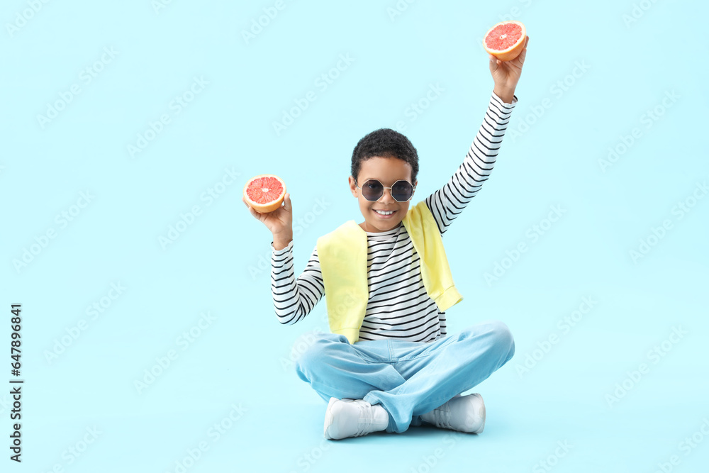 Little African-American boy with slices of grapefruit sitting on blue background