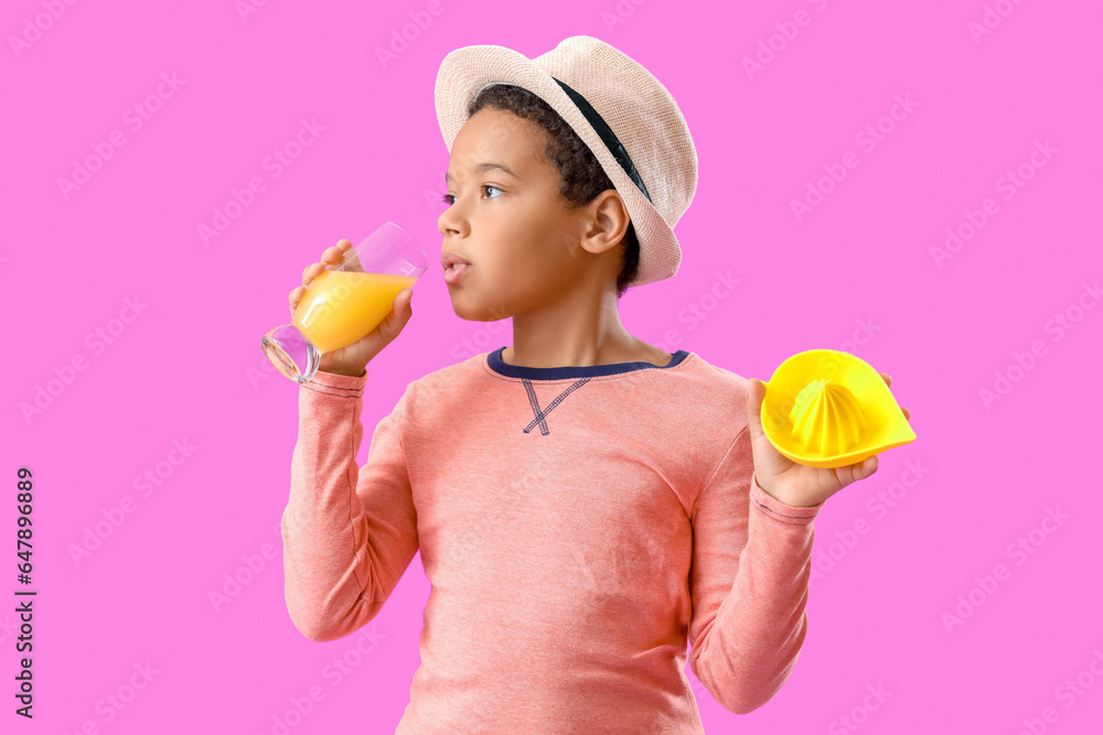 Little African-American boy with glass of fresh citrus juice and squeezer on purple background