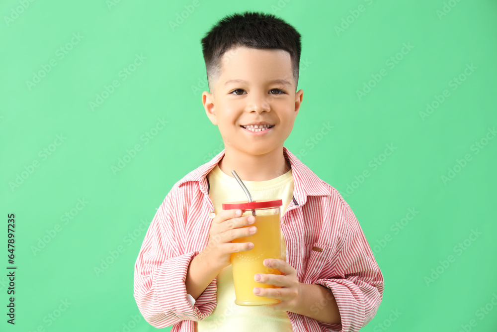 Little Asian boy with cup of fresh citrus juice on green background