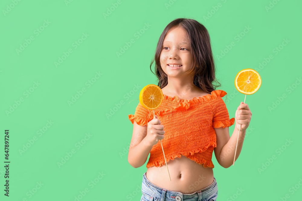 Little Asian girl with slices of orange on sticks against green background