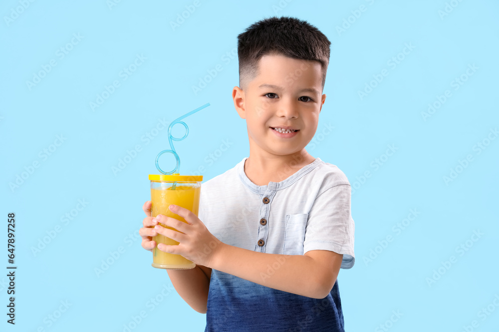 Little Asian boy with cup of fresh citrus juice on blue background