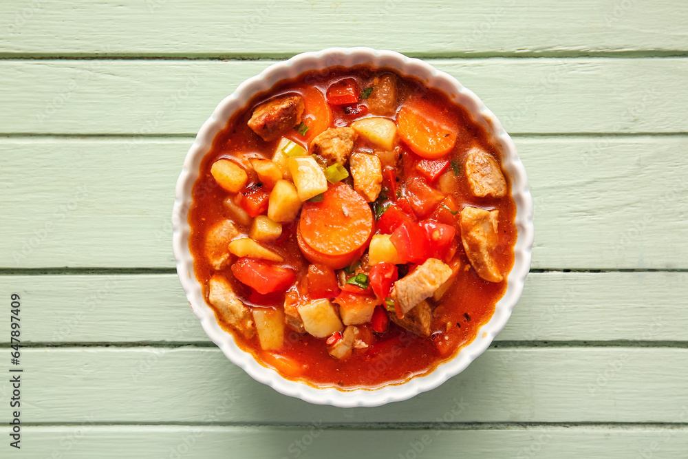 Bowl of tasty beef stew on green wooden background