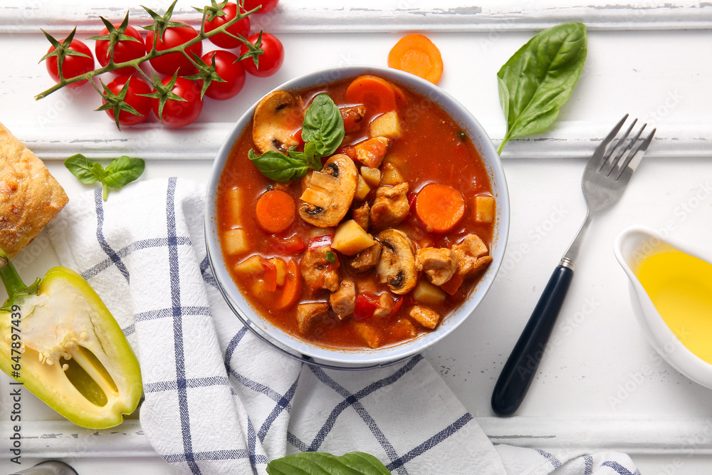 Bowl of tasty beef stew and ingredients on white wooden background