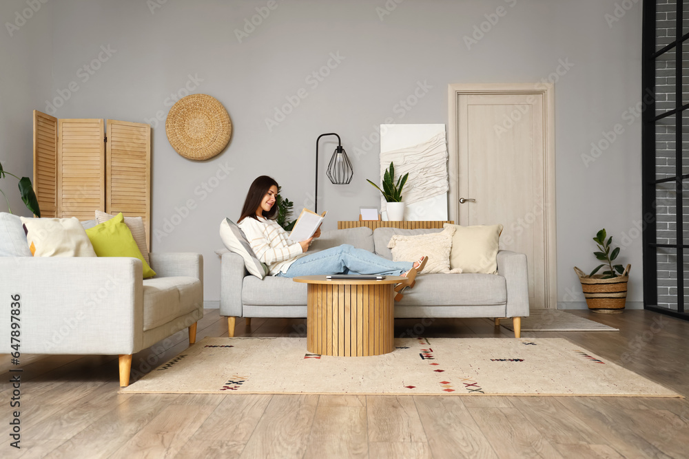 Young woman reading book on sofa in living room