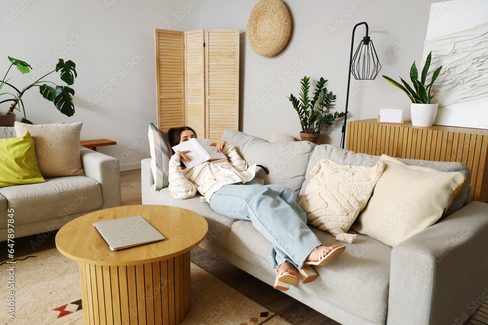 Young woman reading book on sofa in living room