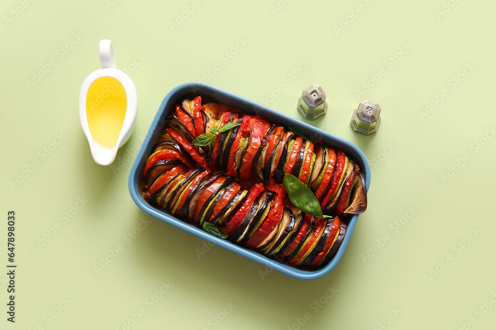 Baking dish of tasty Ratatouille, spices and gravy boat with oil on green background