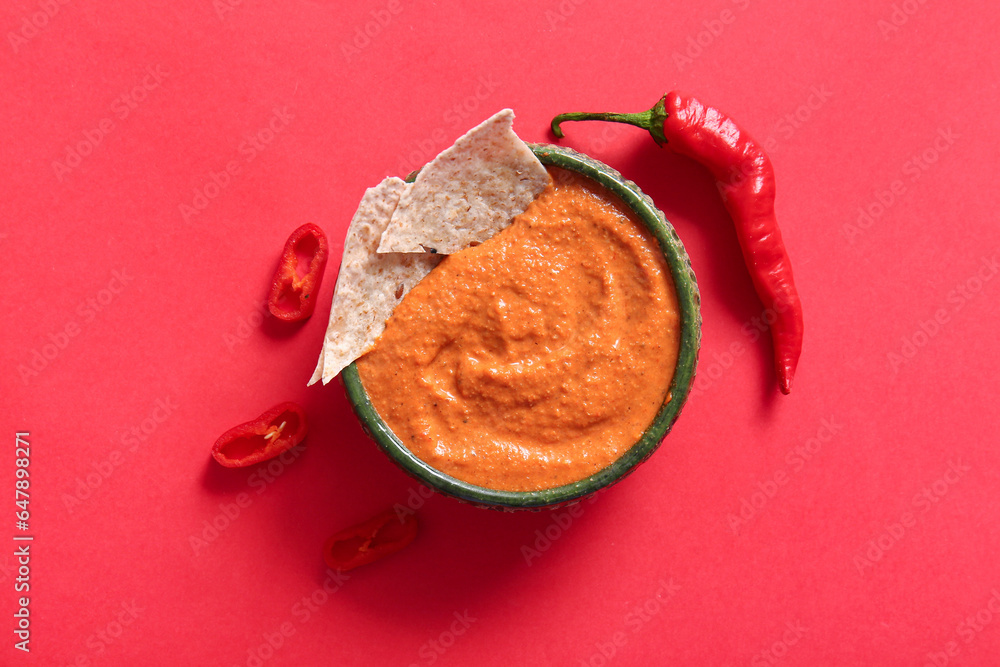 Bowl of tasty muhammara and chili peppers on red background