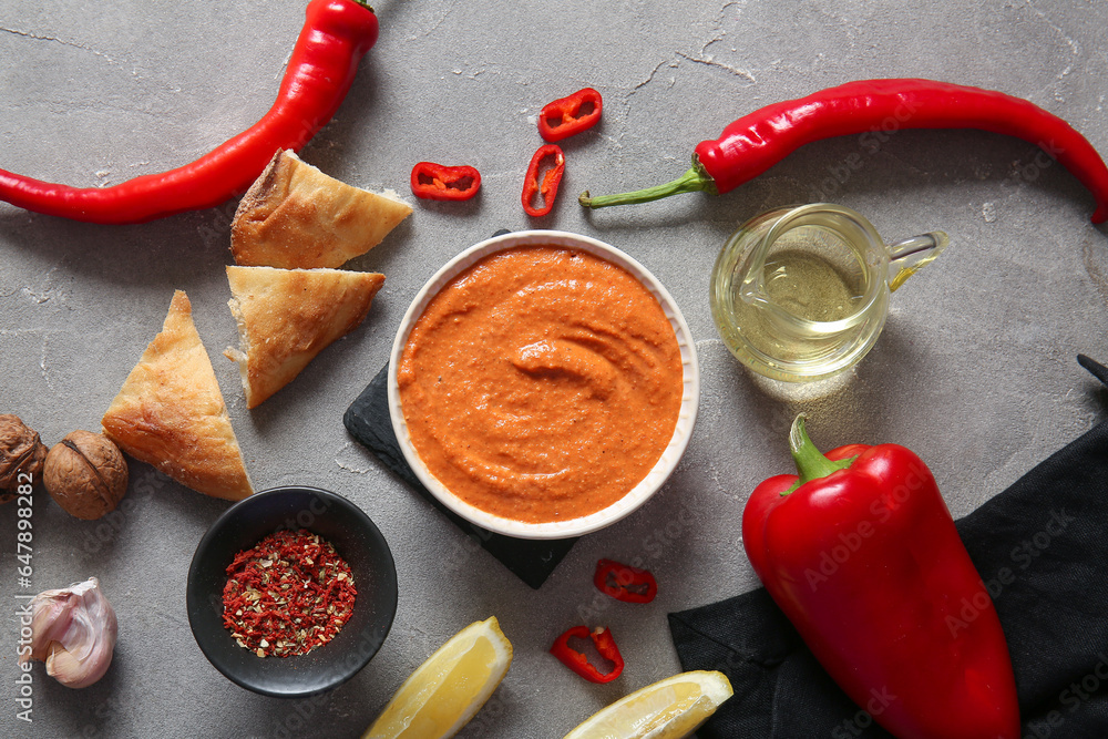 Bowl of tasty muhammara and ingredients on grey background