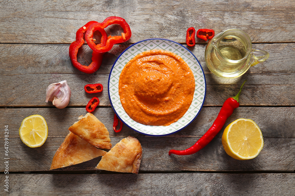 Plate of tasty muhammara and ingredients on wooden background