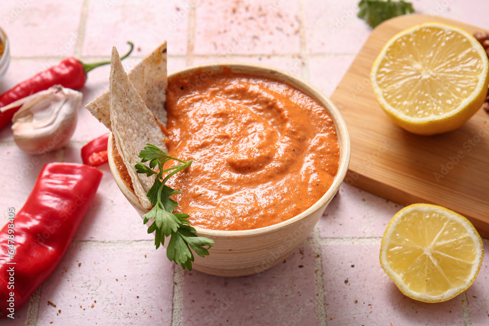 Bowl of tasty muhammara and ingredients on pink tile background