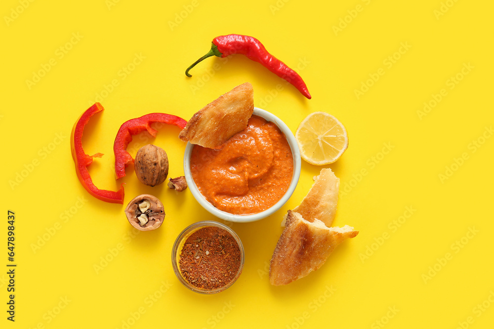 Bowl of tasty muhammara and ingredients on yellow background