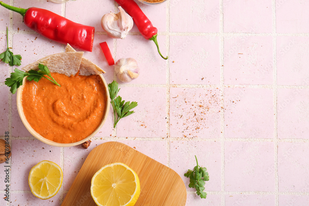 Bowl of tasty muhammara and ingredients on pink tile background