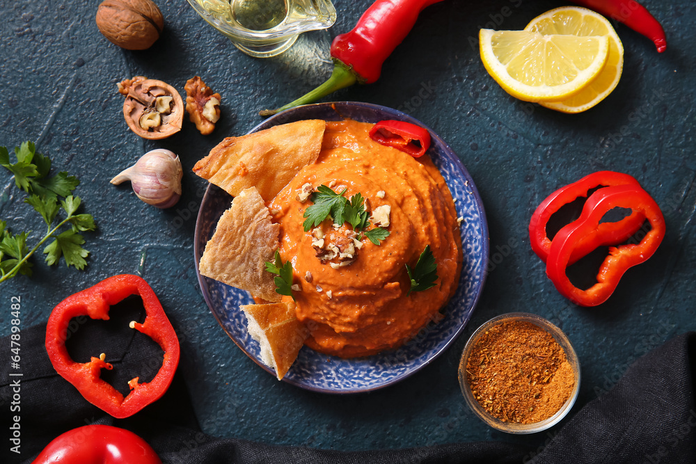 Plate of tasty muhammara and ingredients on black background