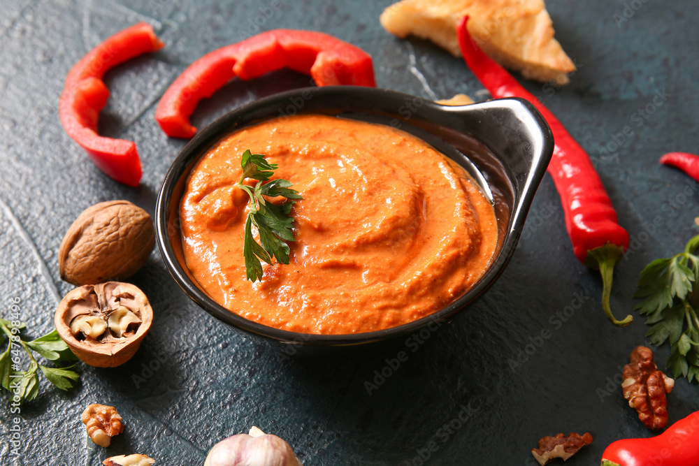 Bowl of tasty muhammara and ingredients on black background