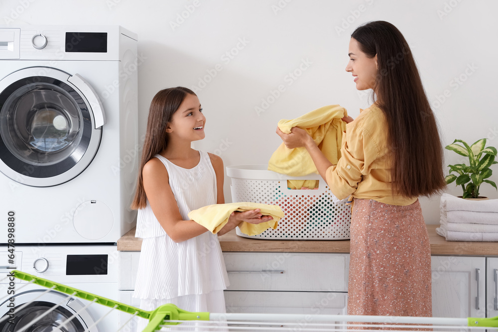 Happy mother with her little daughter doing laundry at home