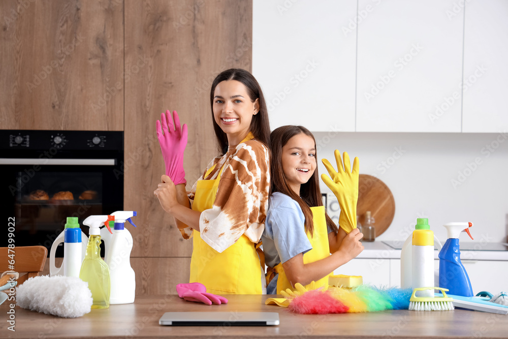 Happy mother with her little daughter putting rubber gloves for cleaning in kitchen