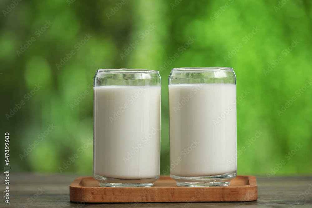 Board with glasses of fresh milk on wooden table outdoors