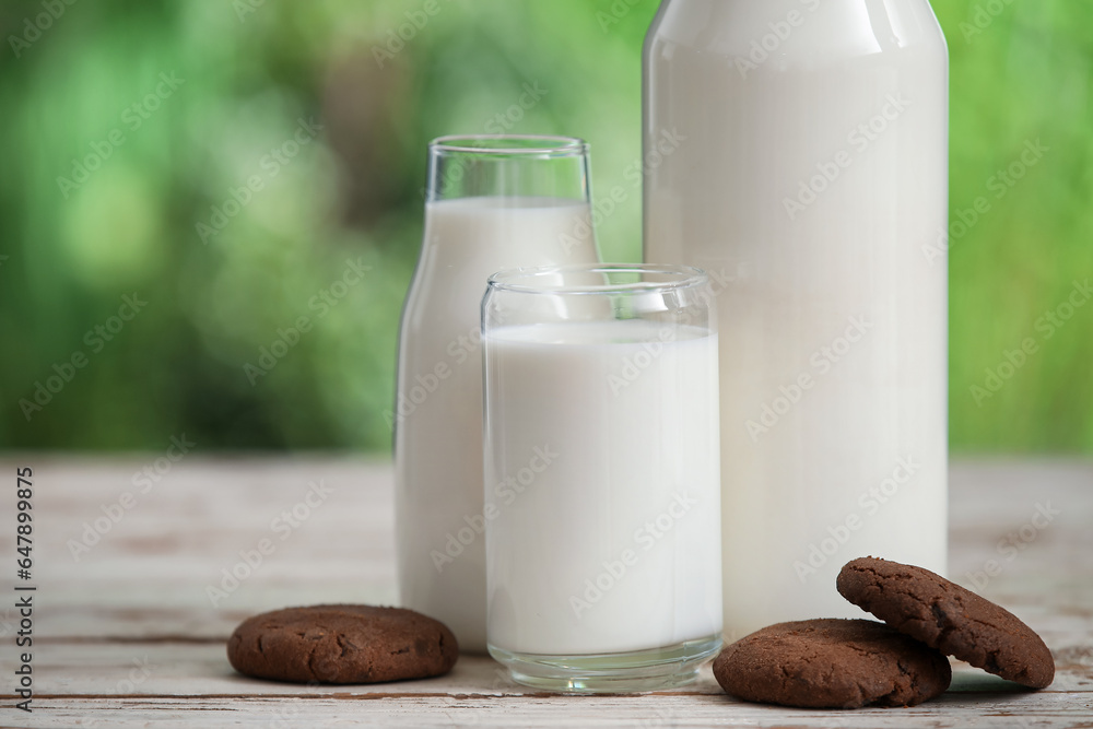 Glass and bottles of fresh milk with sweet cookies on white wooden table outdoors