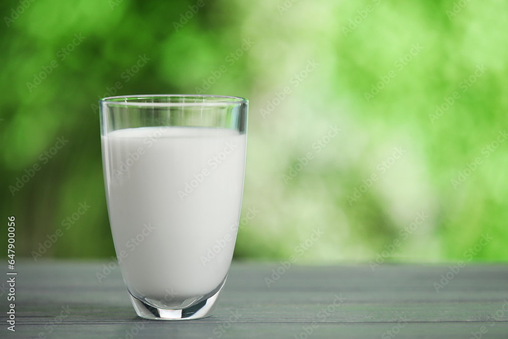 Glass of fresh milk on grey wooden table outdoors