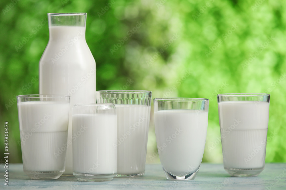 Glasses and bottle of fresh milk on blue table outdoors