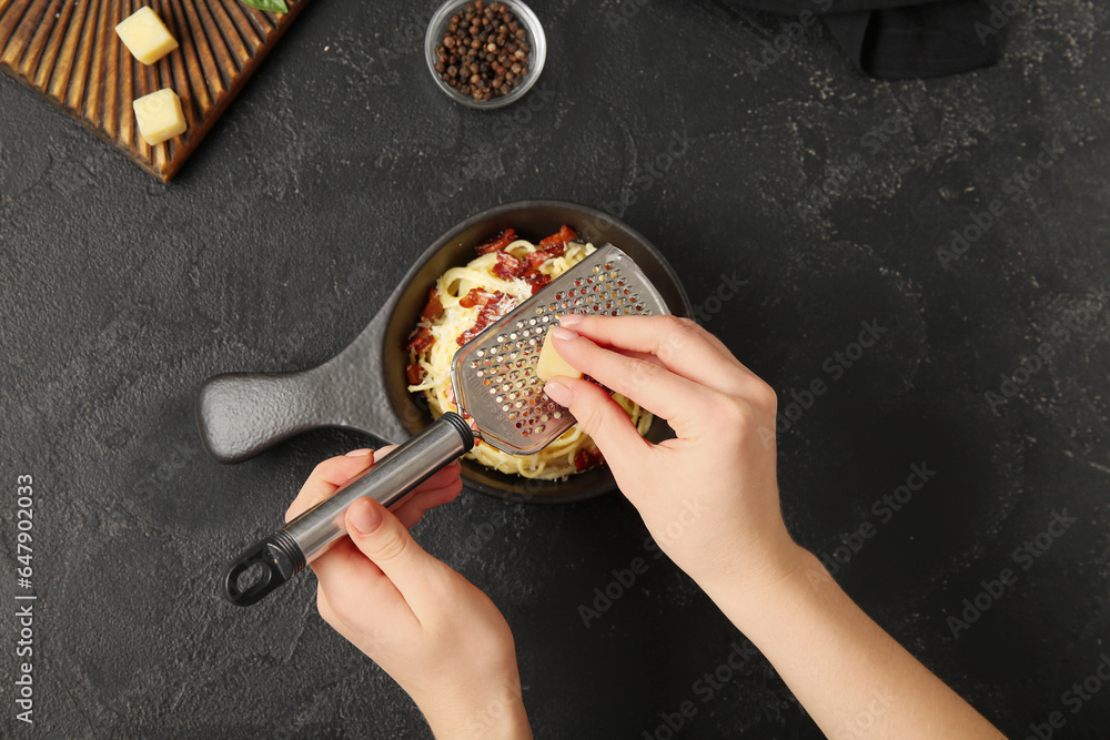 Woman adding cheese into frying pan with tasty pasta carbonara on black background