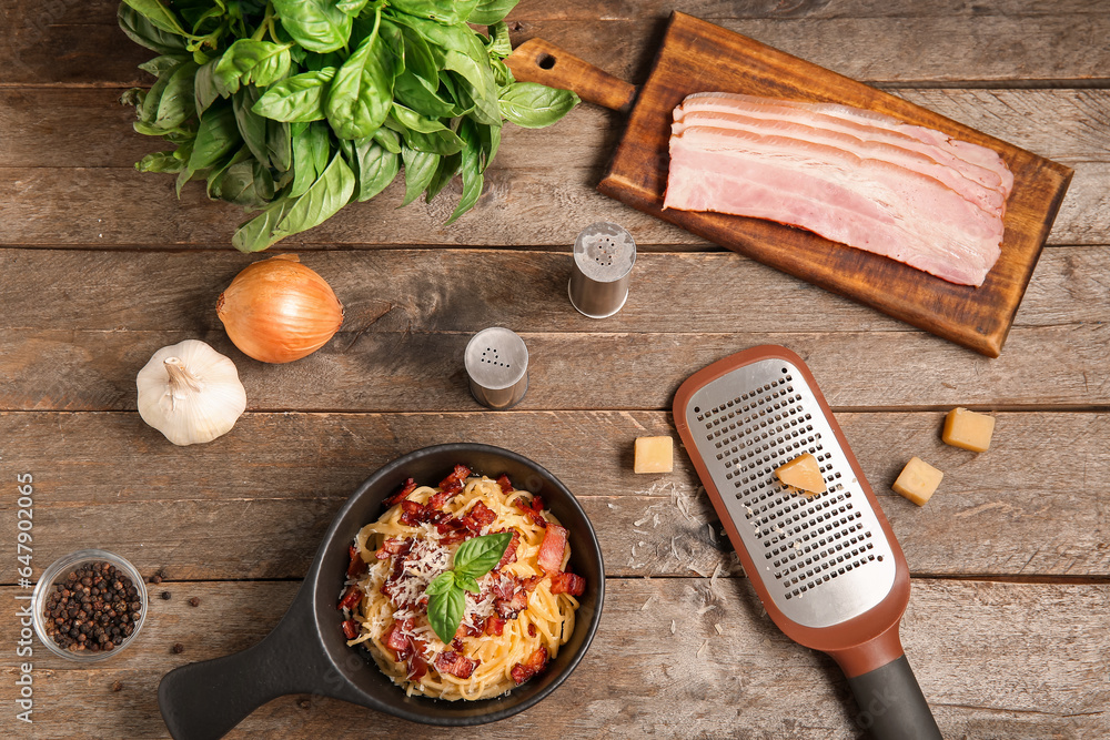 Frying pan with tasty pasta carbonara and ingredients on wooden background