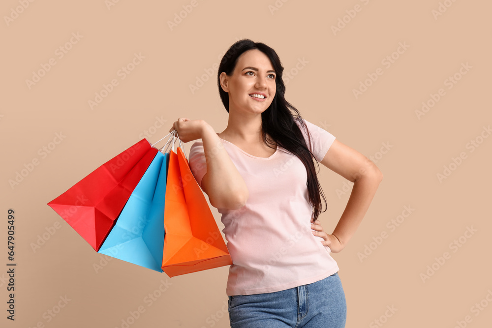 Beautiful happy woman with shopping bags on beige background