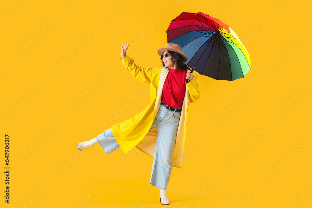 Stylish young Asian woman in fall clothes with umbrella on yellow background