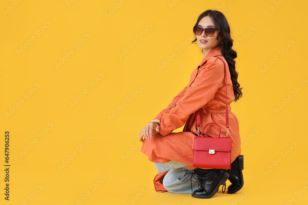 Stylish young Asian woman in fall clothes on yellow background