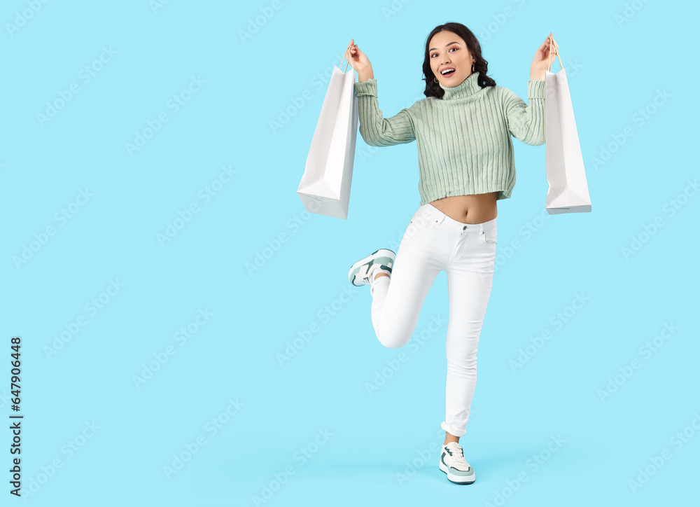 Happy young Asian woman with shopping bags on blue background