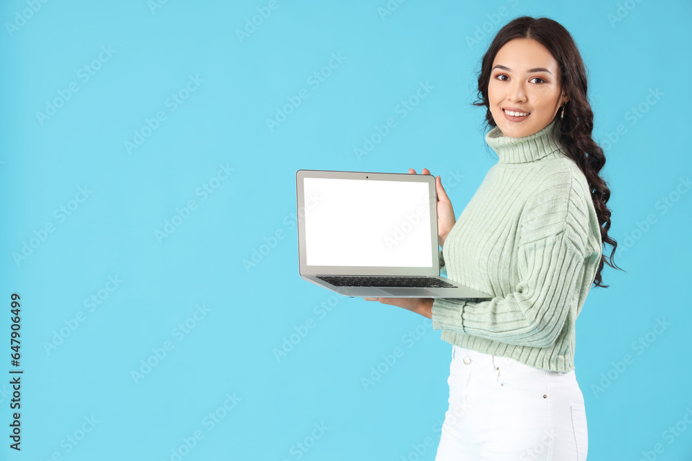 Young Asian woman with laptop on blue background