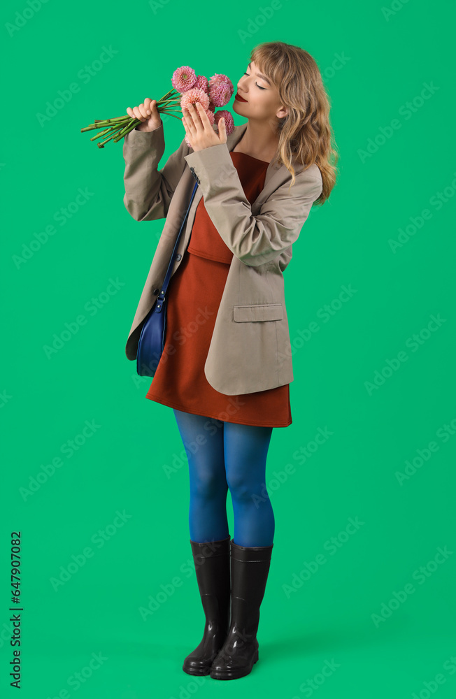 Stylish young woman in fall clothes with flowers on green background