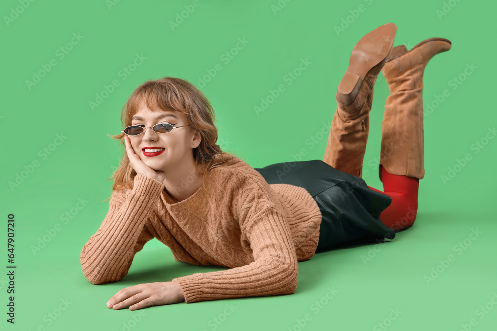 Stylish young woman in fall clothes lying on green background