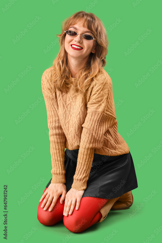 Stylish young woman in fall clothes sitting on green background