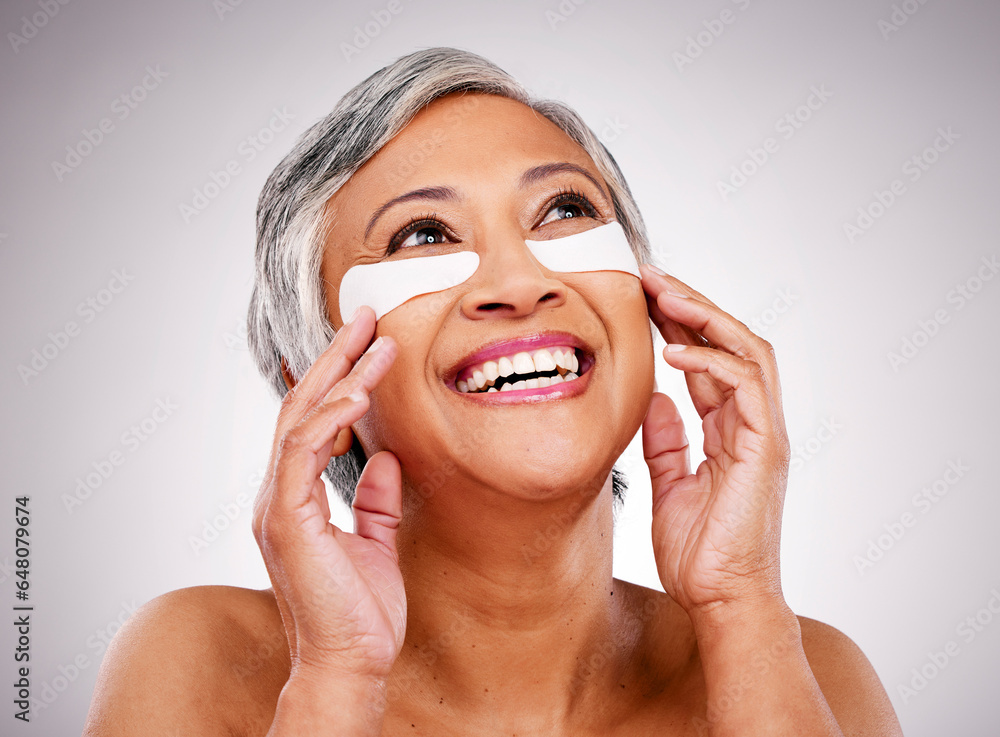 Senior, happy woman and face with eye patches in skincare, cosmetics or anti aging against a studio background. Mature female person or model smile with pads on eyes for facial treatment or routine