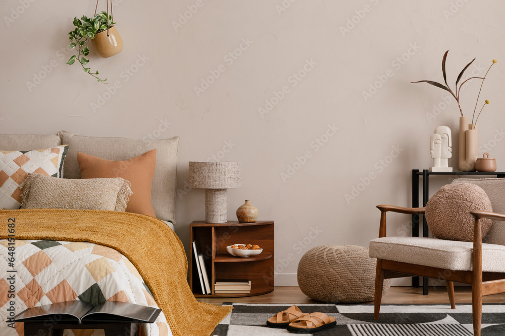 Interior design of warm bedroom with mock up poster frame, black rack, bed with orange bedding, stylish armchair, round pillow, patterned rug, slippers and personal accessories. Home decor. Template.