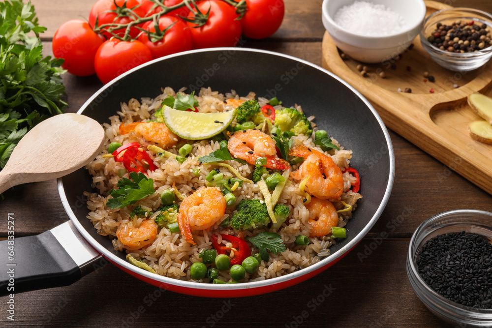 Tasty rice with shrimps and vegetables in frying pan on wooden table, closeup