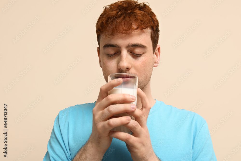 Young man with glass of milk on beige background