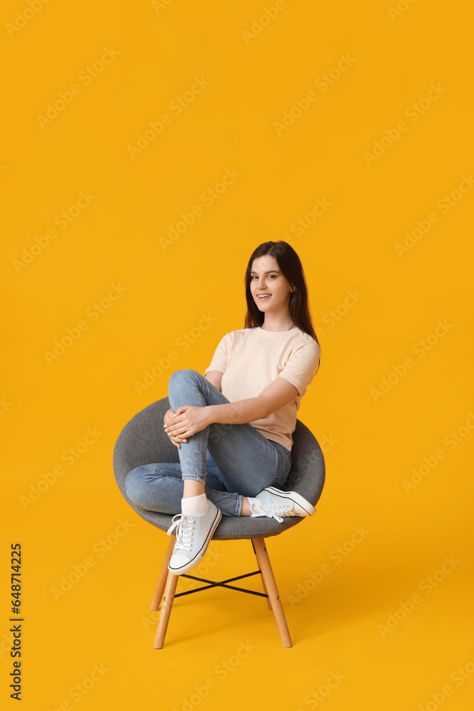 Young woman sitting in armchair on yellow background