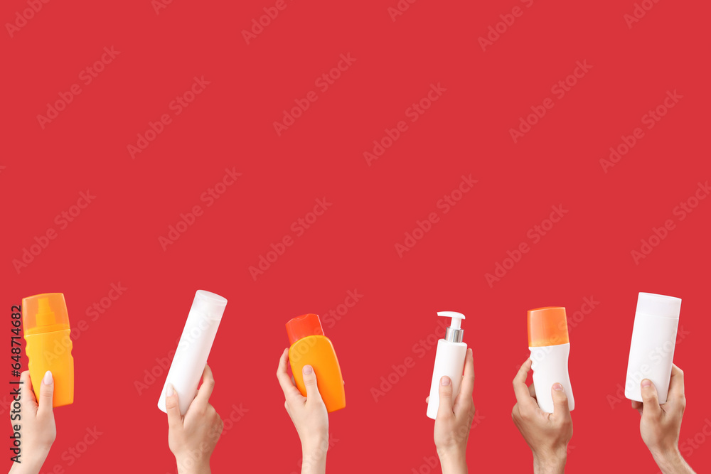 Female hands with bottles of sunscreen cream on red background