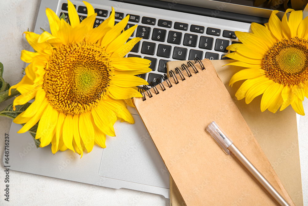 Modern laptop, sunflowers and notebooks on light background