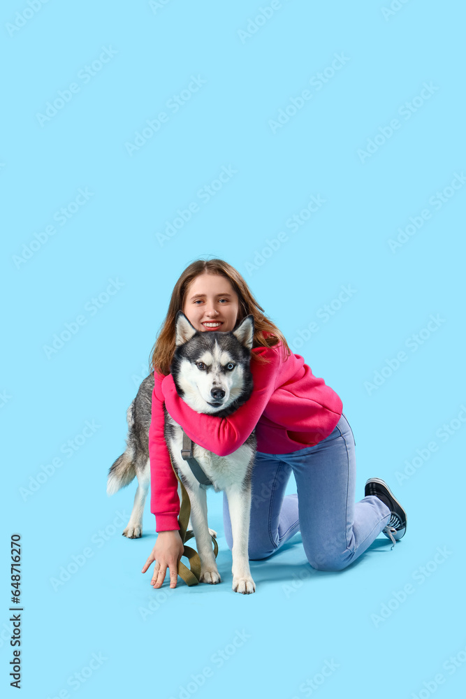 Happy young woman with husky dog on light blue background