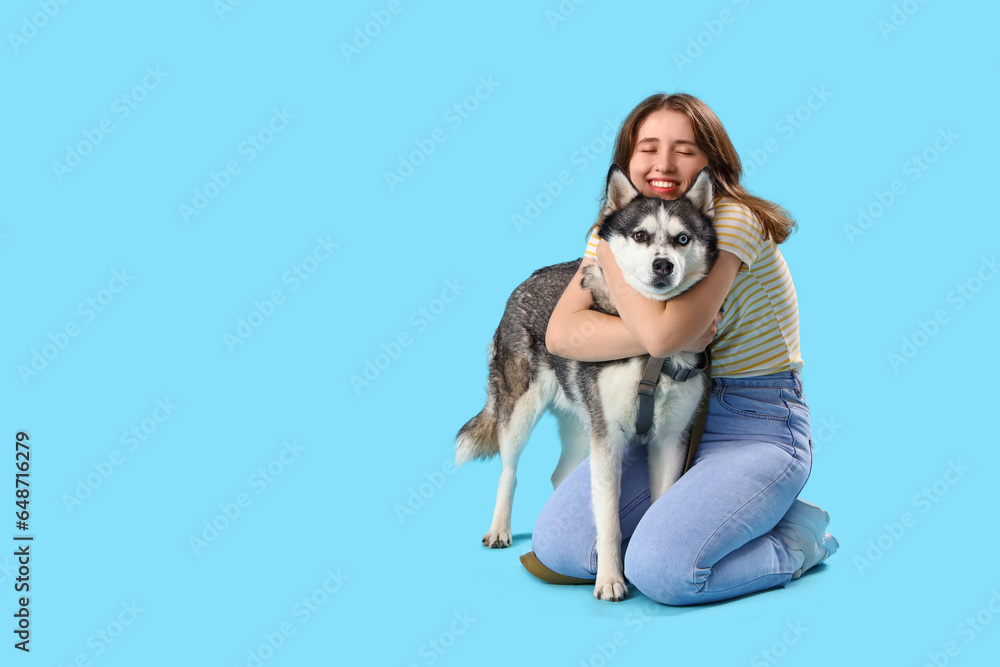 Happy young woman with husky dog on light blue background