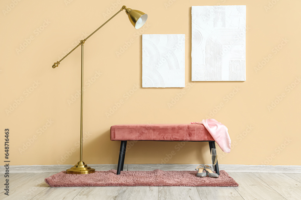 Paintings, standard lamp and pink bench near beige wall