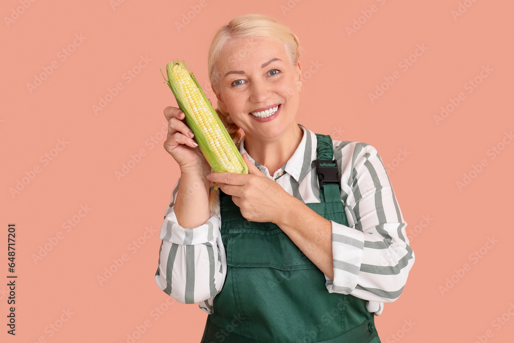 Mature female farmer with ripe corn cob on orange background