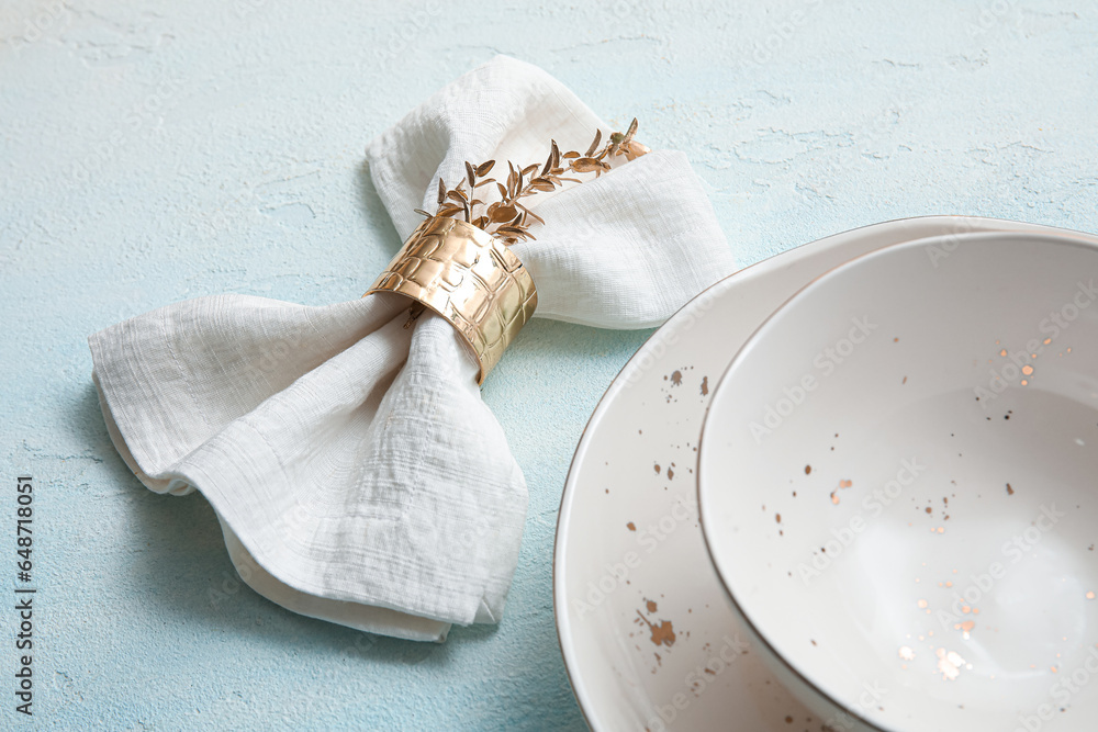 Napkin with golden leaves and clean dishes on light blue table, closeup