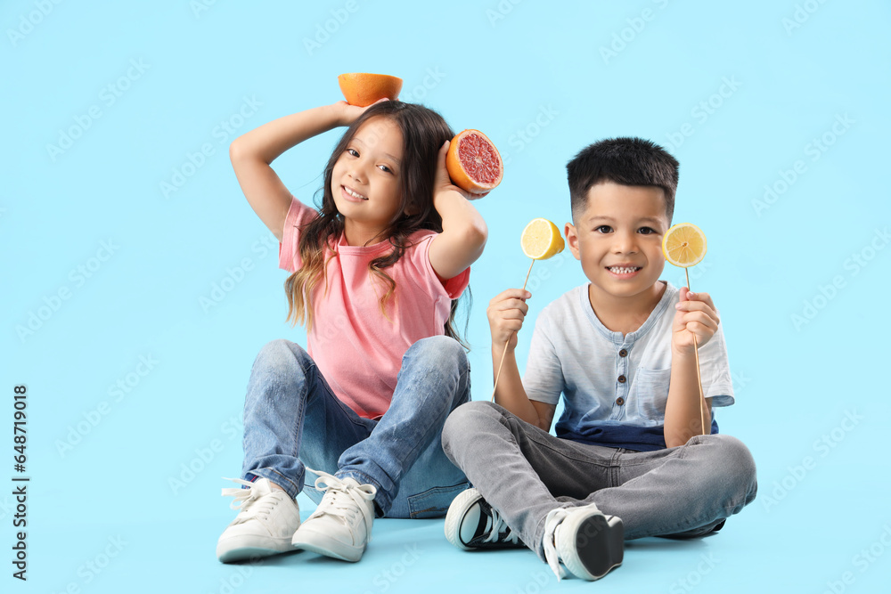 Little Asian children with slices of fresh citruses sitting on blue background